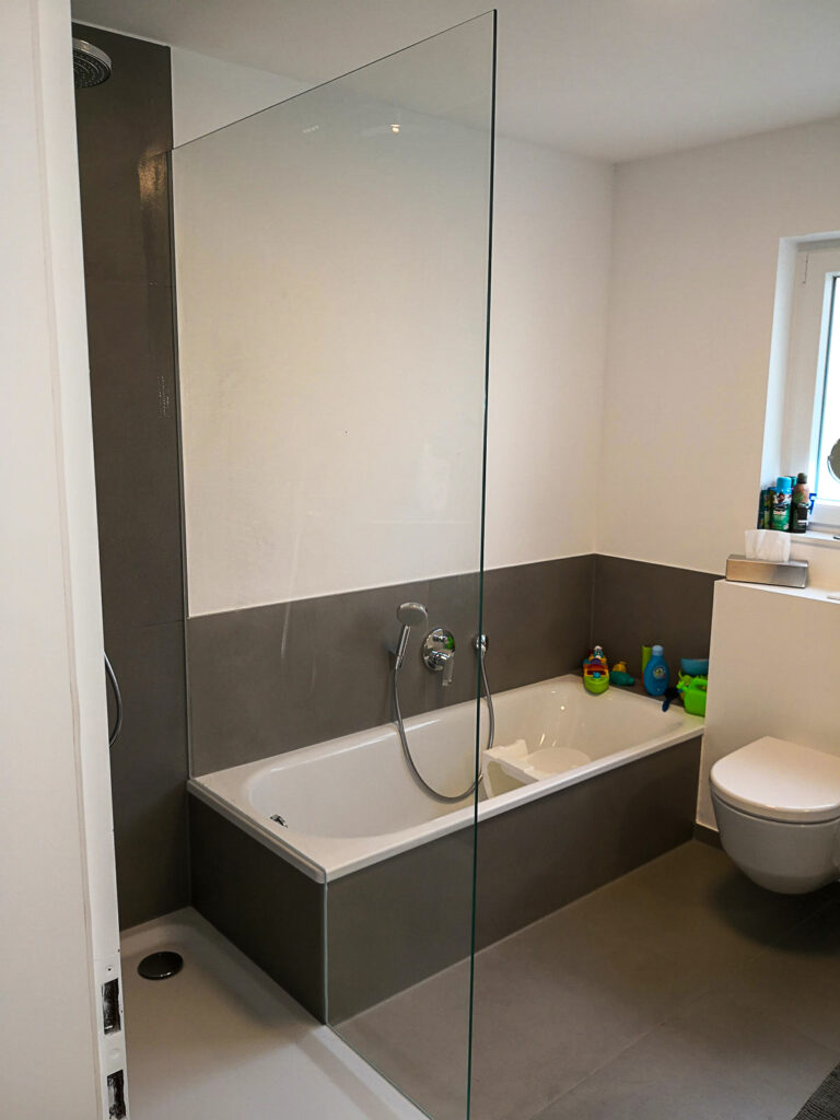 Glas-Duschwand mit Badewanne im Hintergrund